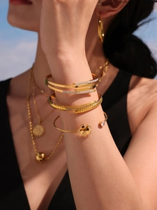 Detail of gold clover bangle and nail bracelet with zircon inlay on a female wrist