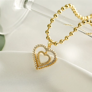 Detailed macro view of gold heart double pendant with zircons and beaded chain on silk