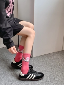 Detail of pink crew socks featuring white YEAH letters and heart patterns on the model