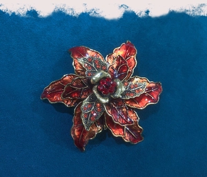 Detailed close-up of vintage deep red flower brooch with gold edges on navy velvet