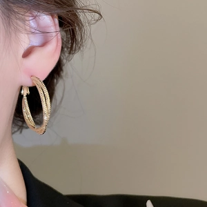 Detailed close-up of textured gold hoop earrings featuring a stylish double intertwined design