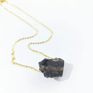 Macro shot of irregular natural dark crystal pendant with a sleek gold chain necklace