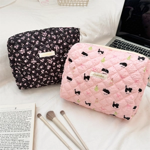 Detailed view of quilted makeup bags with floral and cat patterns on white bedding