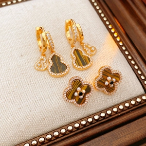 Detailed shot of golden earrings with tiger eye stone, pearls and clover design
