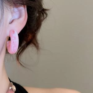 Close-up of a pink resin C-shaped hoop earring with white marble texture on a model