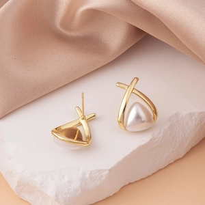 Macro detail of gold crisscross stud earrings featuring a triangle pearl on white rock