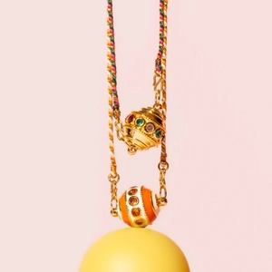 Detail of a gold hollow ball pendant with orange enamel beads on a woven lanyard