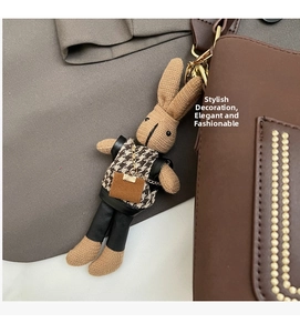 Detail of knitted rabbit charm with houndstooth vest and metal chain on brown bag