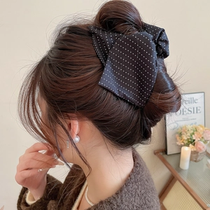 Detail showing a large black polka dot bow hair clip styled on an elegant updo hairstyle