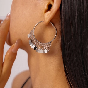Detail view of silver hoop earrings with hanging metal discs on a female model