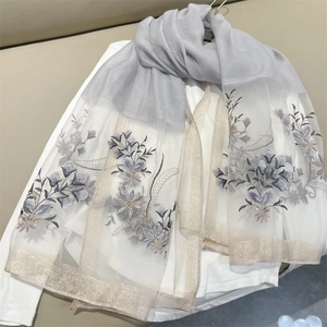 Detailed close-up of light grey scarf with elegant blue floral embroidery and tulle edges