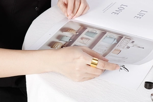 Close-up of a wide gold stainless steel ring worn by a model holding a book