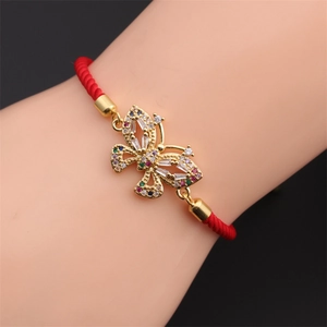 Dettaglio macro del ciondolo a farfalla dorata con zirconi colorati su bracciale rosso