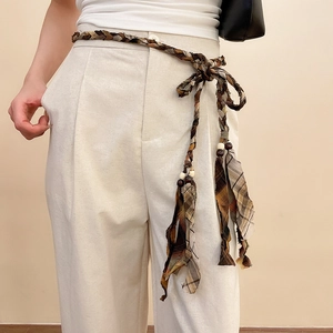 Detail of woven lattice waist chain with wooden beads and tassels on white pants