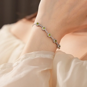 Detail of elegant silver bracelet with green round zircons worn on wrist with tulle background