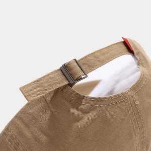 Detail of adjustable metal buckle and red label on khaki cotton twill baseball cap