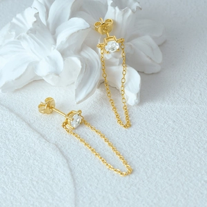 Detail of gold pearl earrings with dangling chains and sparkling crystals on white flower