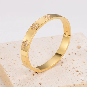 Detail of gold clover bangle with zircon inlays on a travertine stone surface