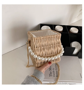Detail of hand-woven straw bag featuring large pearl handle and gold chain strap