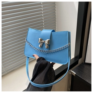 Close-up of sky blue shoulder bag with silver metal bow and delicate chain detail