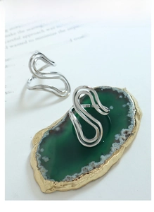 Close-up of elegant silver S-shaped wave rings on green agate stone and magazine page