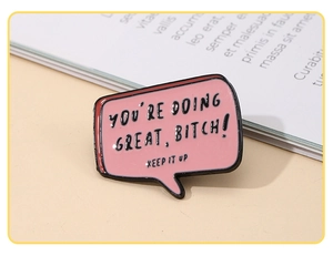 Detail of a pink enamel speech bubble brooch with encouraging text on a book background