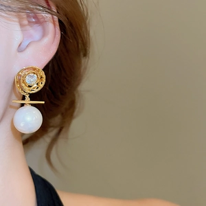 Macro detail of gold swirl earring with zircon center and large white pearl drop