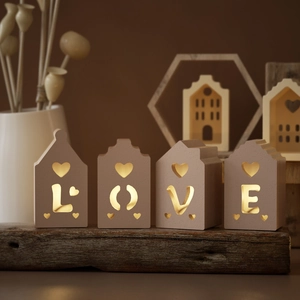 Detailed view of warm glowing LOVE letters and heart cutouts on house-shaped tea light holders