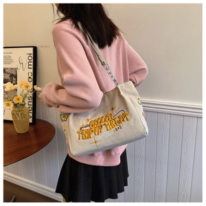 Detail of embroidered canvas tote bag with chain strap shown in a casual lifestyle setting