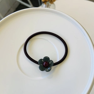 Élastique à cheveux fleur vert foncé avec bandeau noir sur assiette blanche