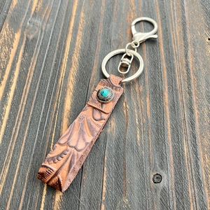 Close-up of vintage brown leather keychain with embossed patterns and turquoise stone