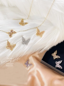 Detailed close-up of 14k gold plated butterfly pendants with zircon inlay on satin fabric
