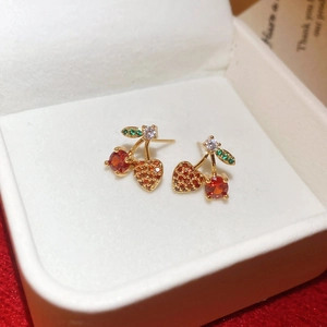 Detail view of cherry stud earrings with red zircons and gold leaf on red velvet