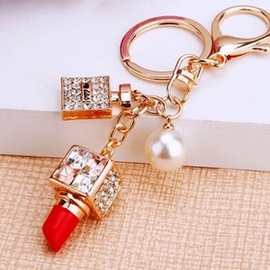 Detail of a golden keychain with red lipstick charm and crystal perfume bottle