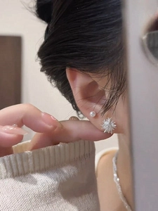 Close-up of minimalist dandelion pearl studs and silver snowflake earrings on ear