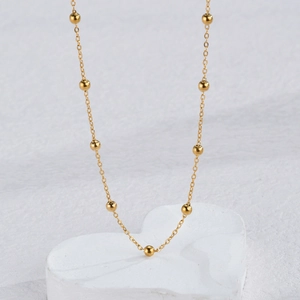 Minimalist gold beaded necklace set on heart-shaped display with a polished metallic finish