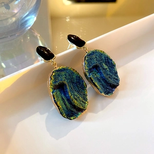 Macro view of blue resin stone earrings with gold edging and black geometric stud