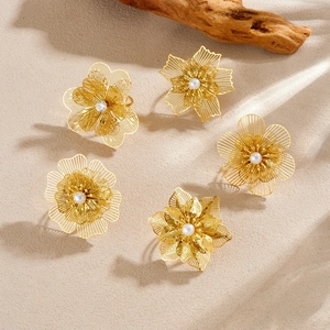 Golden mesh layered petal flower rings set with pearl centers on natural sand background