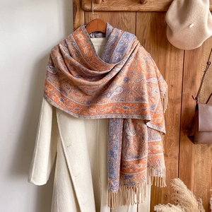 Detail of vintage paisley scarf with orange and blue fringe on a beige coat