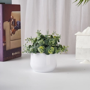 Detailed view of artificial green potted plant in a white round ceramic pot on a desk