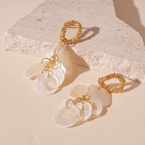 Macro detail of round golden hoop earrings with white shell tassels on a stone surface
