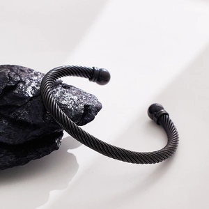 Detail of a black twisted steel cable cuff bracelet with bead ends on a dark rock surface