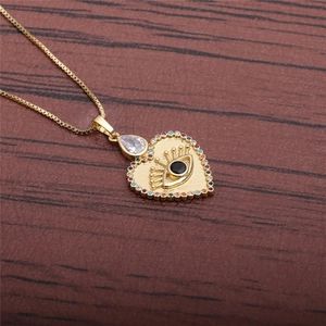 Golden heart necklace with colorful zircon devil eye pendant on a dark wood background