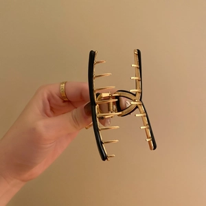 Elegant gold and black metal hair claw clip in a bow design held by a hand