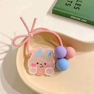 Detail of pink rabbit hair tie with bow and colored beads on a cream display tray