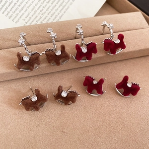 Macro detail of flocked rocking horse earrings with sparkling zircon accents on beige velvet