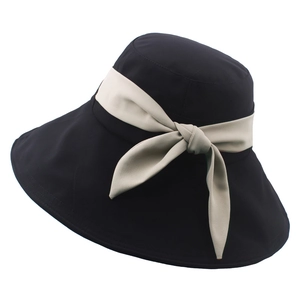Dettaglio di un cappello da sole in tessuto nero con un nastro a fiocco bianco