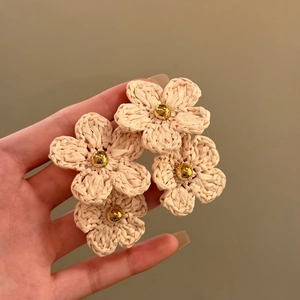 Close-up detail of hand-woven beige flower earrings with golden center bead.