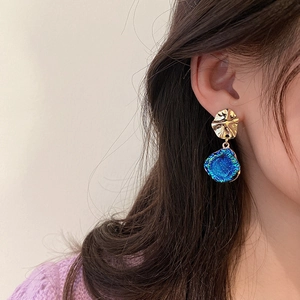 Detail view of gold textured metal earrings with navy blue druzy stone on model
