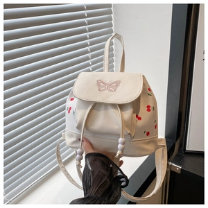 Detail of mini white backpack featuring red cherry prints and pink butterfly embroidery
